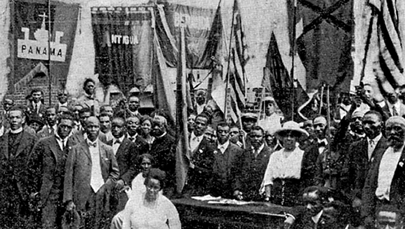 Marcus Garvey standing behind desk with leaders and delegates from various countries at 1920 U.N.I.A. Convention in Harlem, New York